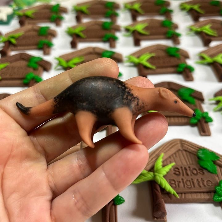 Peça de tamanduá-mirim em biscuit modelada à mão, segurada na mão.